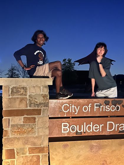 Ethan and a friend sitting on a park sign at dusk